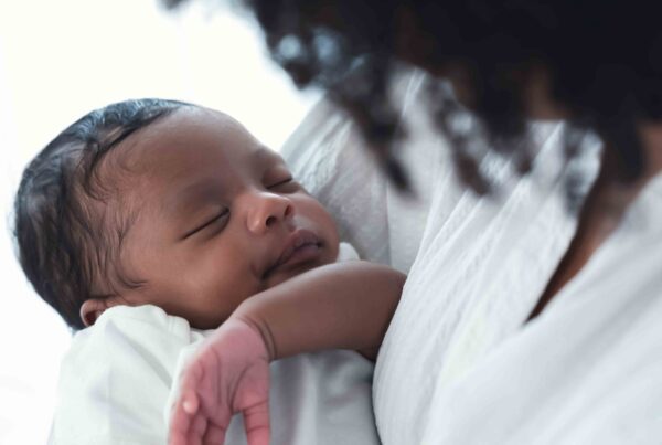 A newborn baby peacefully sleeping in the arms of her mother.