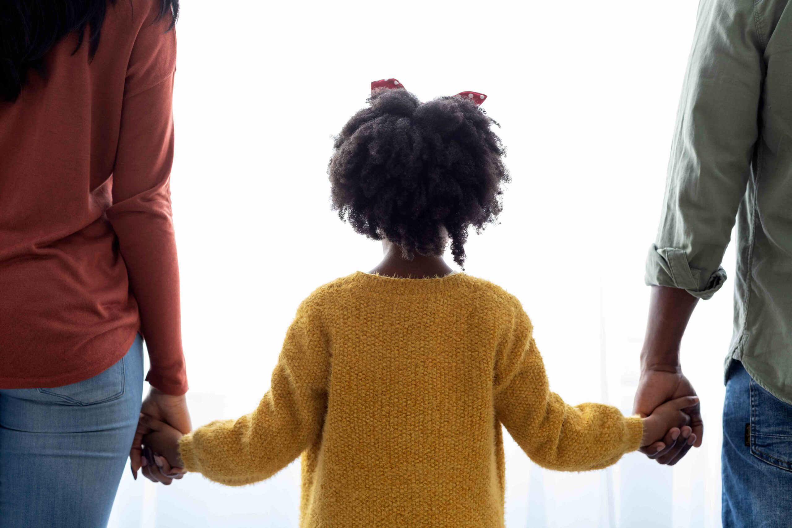 a rear-view of a little girl in the middle, holding her parents' hands, hopeful for a bright future despite her parents' divorce.