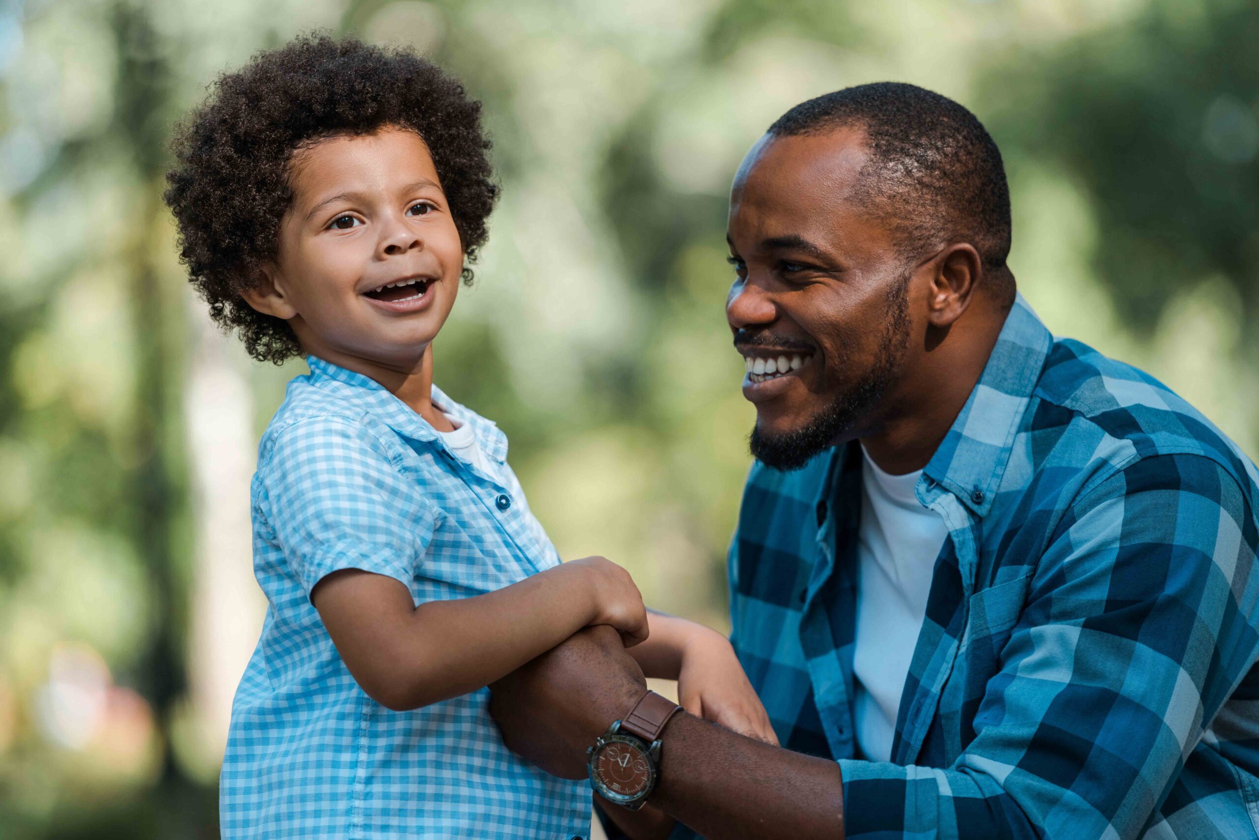 Smiling father and son enjoying a day outdoors, both wearing blue plaid shirts.