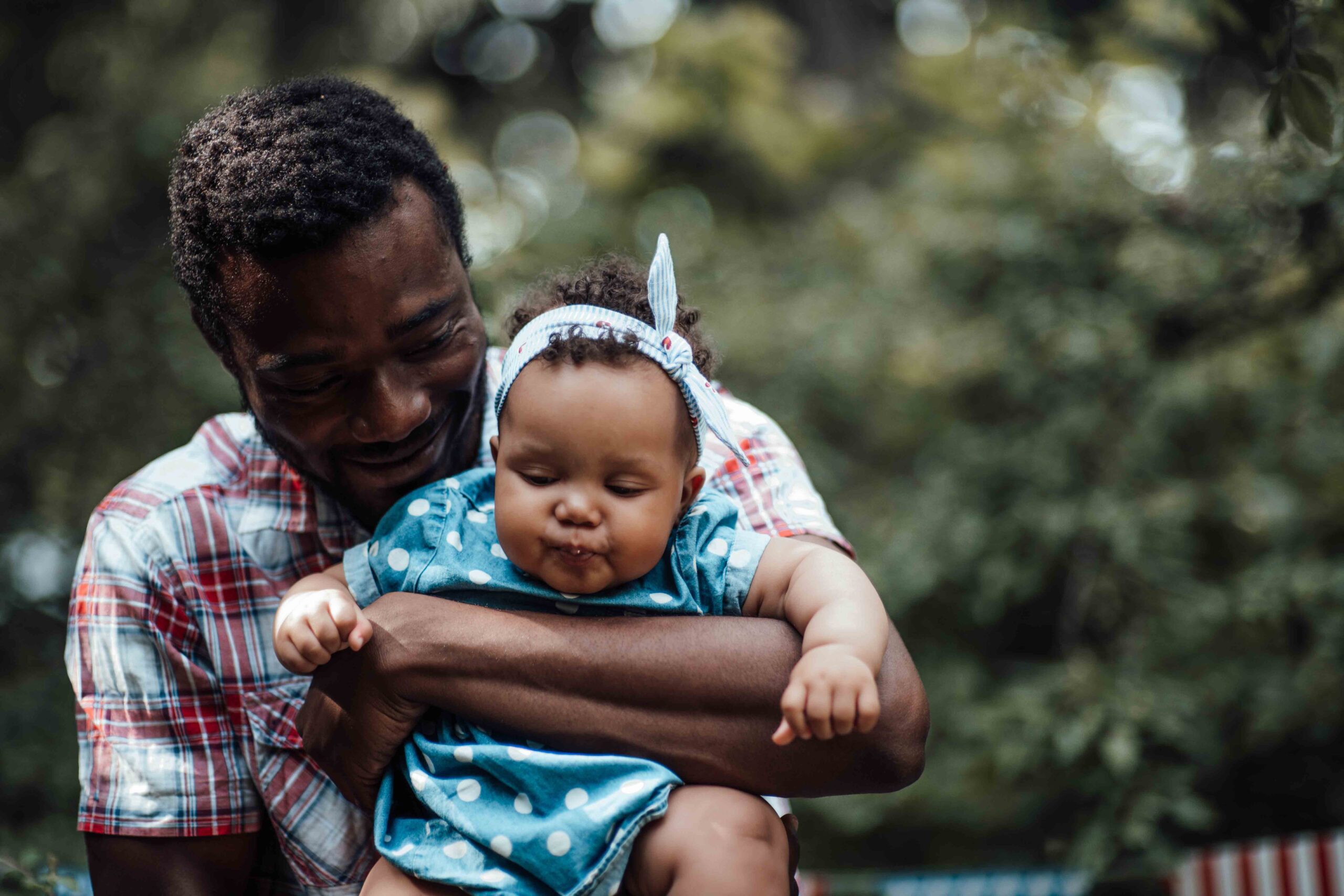 A smiling father holding his baby daughter outdoors, enjoying his child visitation rights.