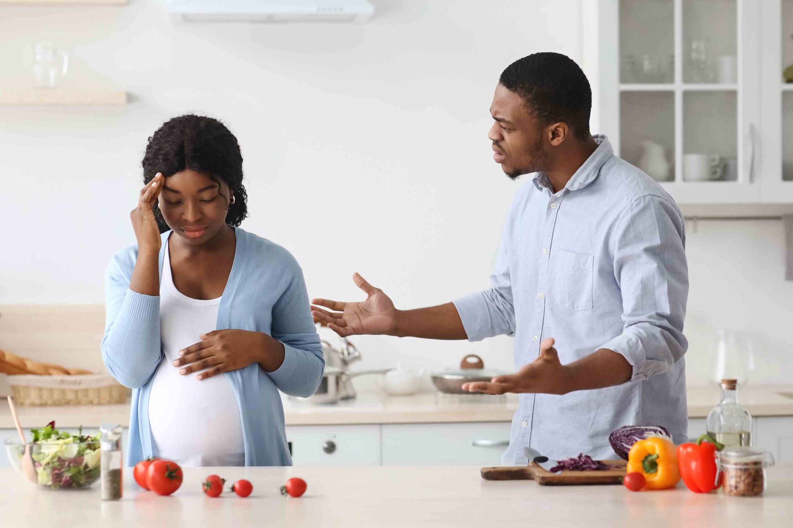 A pregnant woman and a man having a heated discussion in the kitchen, about the father's exclusion from the child's birth certificate