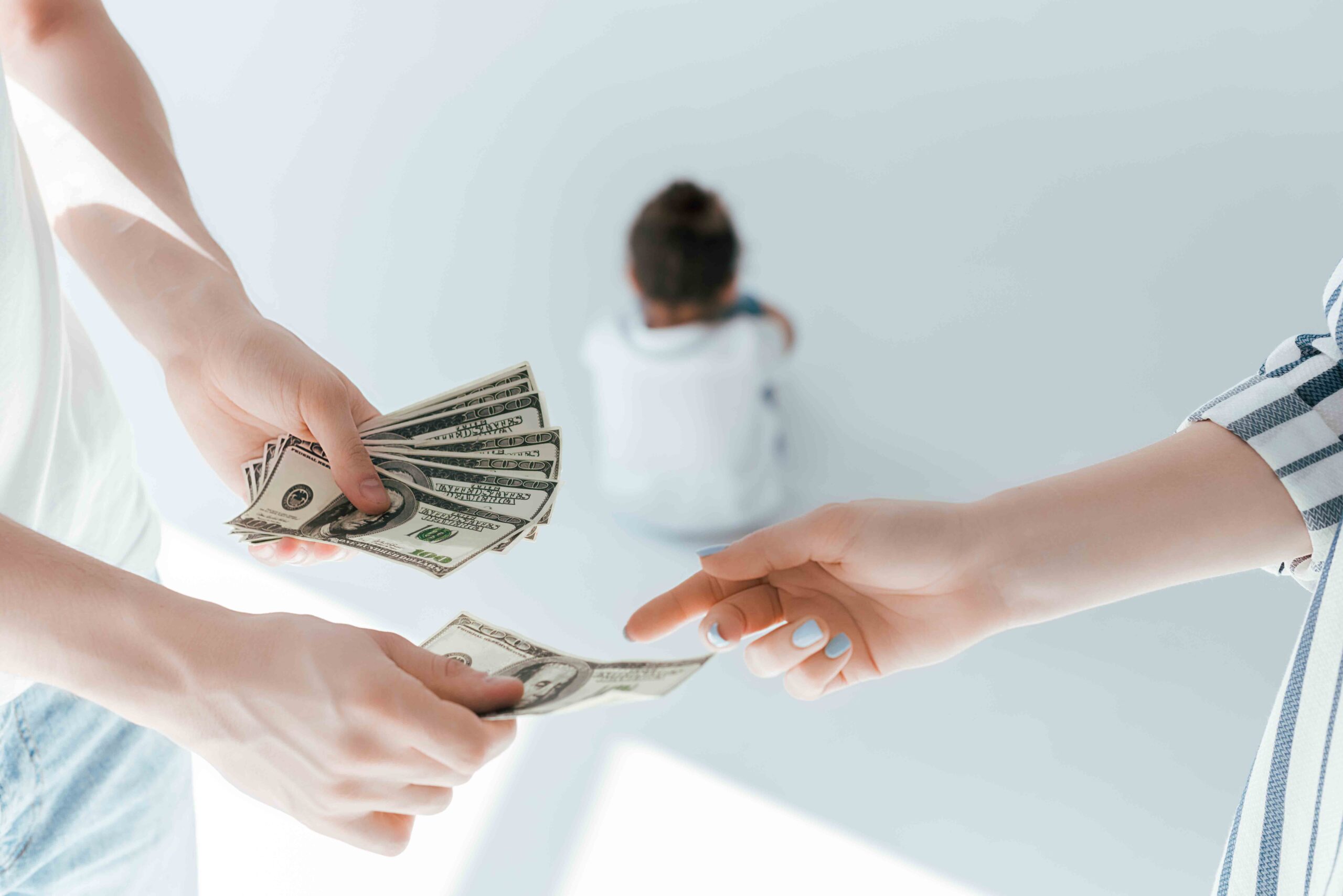 Selective focus of a man giving money to a woman with a child in the background, illustrating the impact of retroactive child support on both parents.