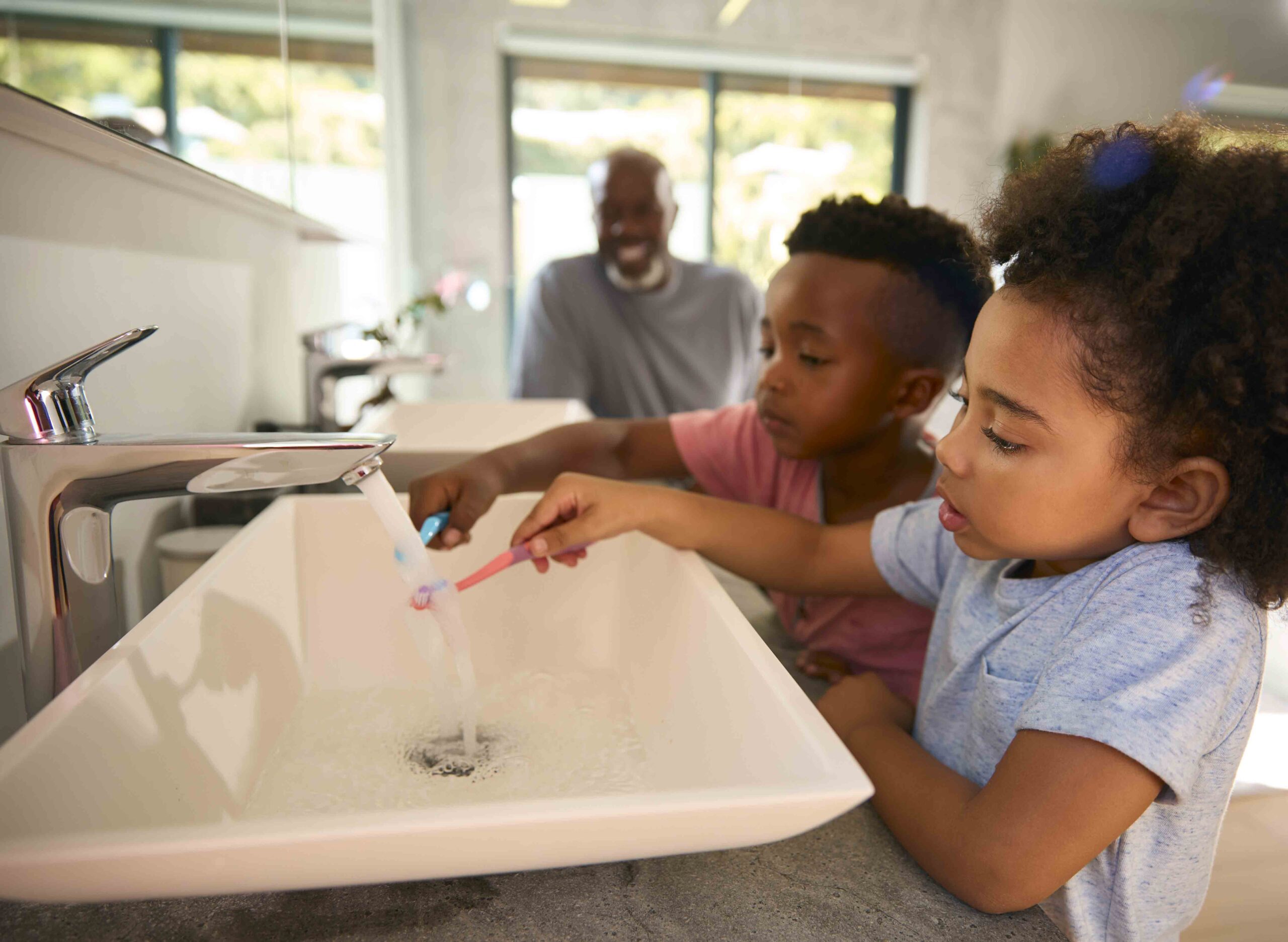 Grandfather helping grandchildren brush teeth in the bathroom, showing the value of guidance despite parent's absence