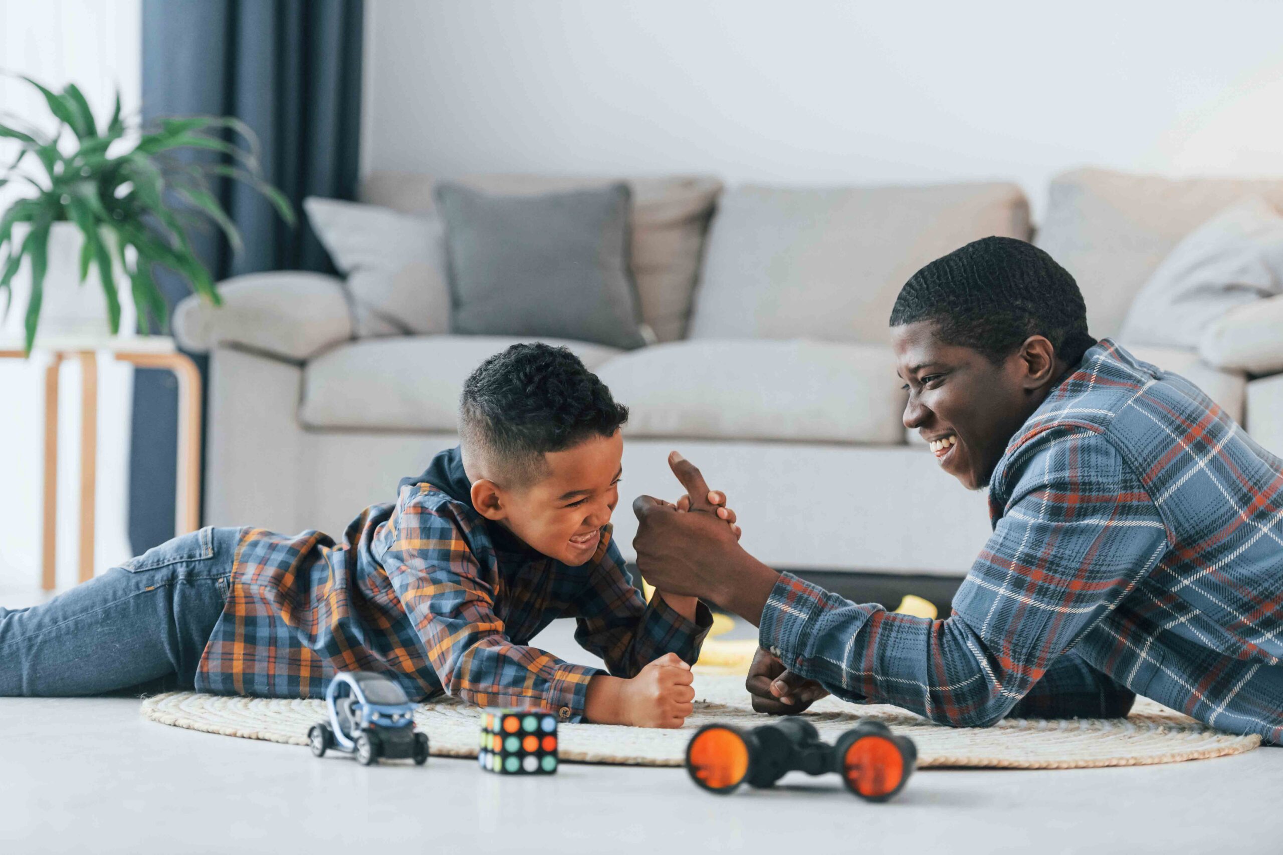 A father playing arm wrestling with his young son at home, illustrating primary and secondary custody roles.