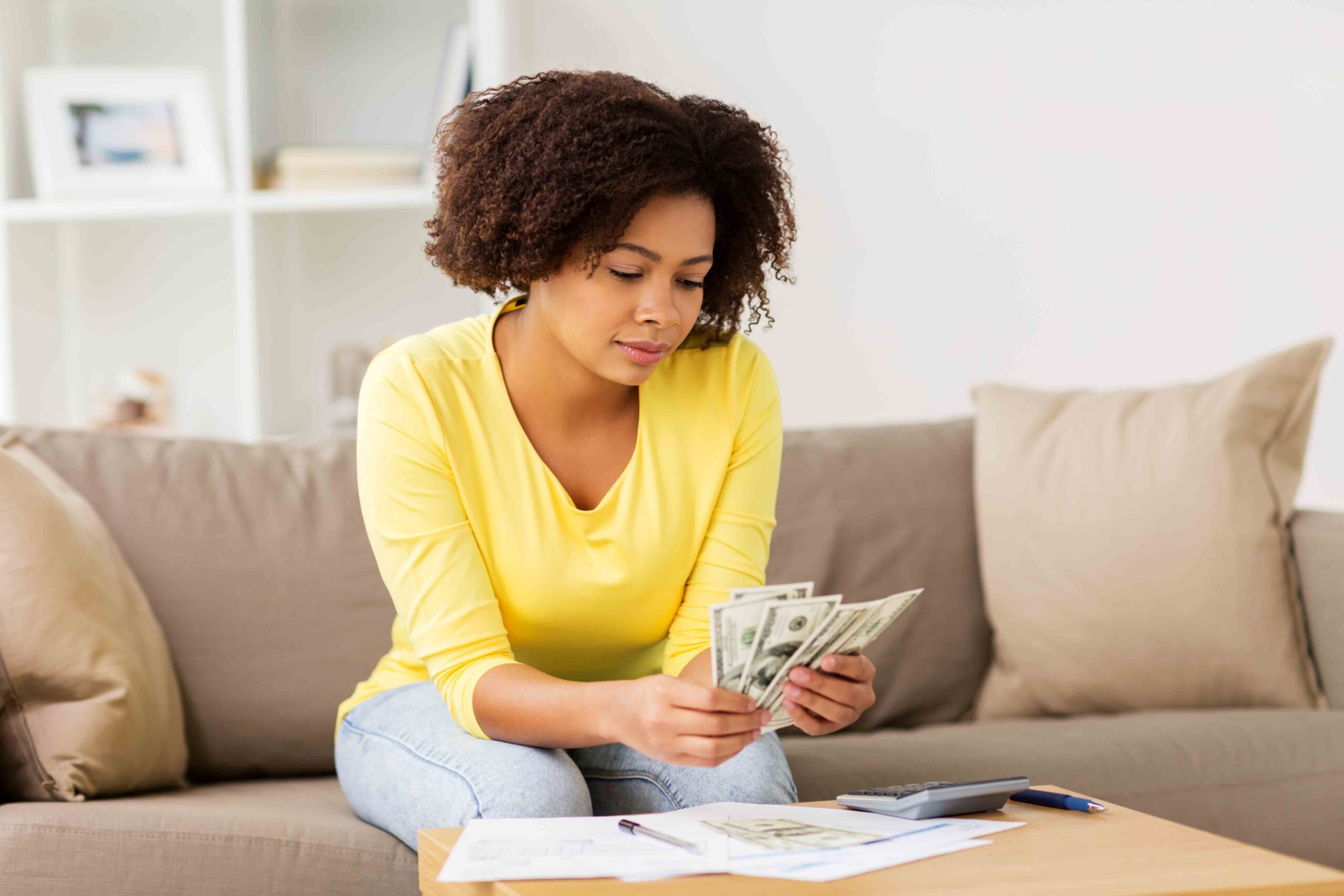 A mother counting money with papers and a calculator, determining financial support for her child at home.