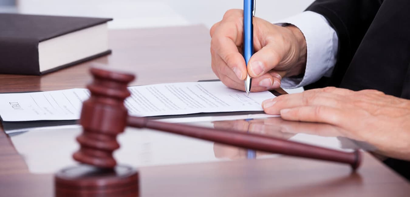 Judge signing a legal document on a desk with a gavel and law book nearby, symbolizing legal proceedings