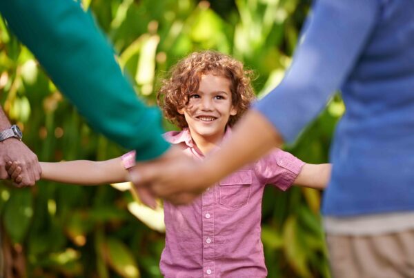 Happy child holding hands with parents, discussing the pros and cons of waiving child support in Texas