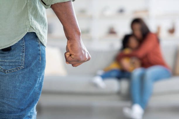 Close-up of a clenched fist with a blurred background of a woman and child, symbolizing domestic violence