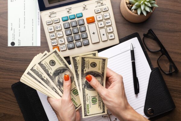 Hands counting dollar bills on a desk with a calculator, checkbook, and financial documents, symbolizing the financial aspect of child support