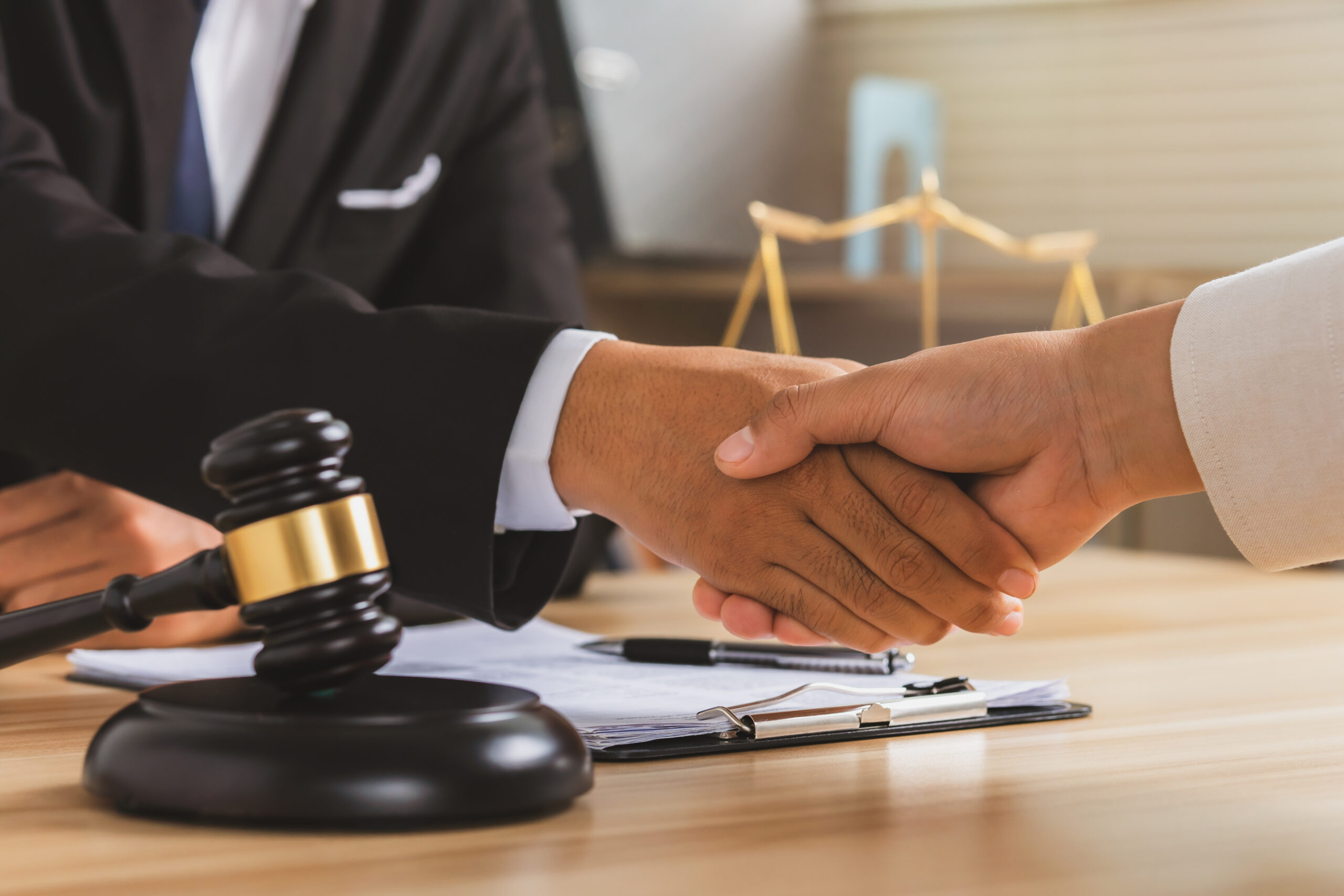 Handshake between a lawyer and a client, with a gavel and legal documents on the table, emphasizing the importance of hiring a divorce attorney