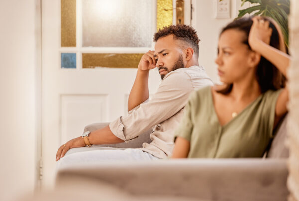 Two individuals sitting apart on a couch, both appearing contemplative and tense, highlighting scenarios where divorce mediation might not be recommended due to communication breakdown