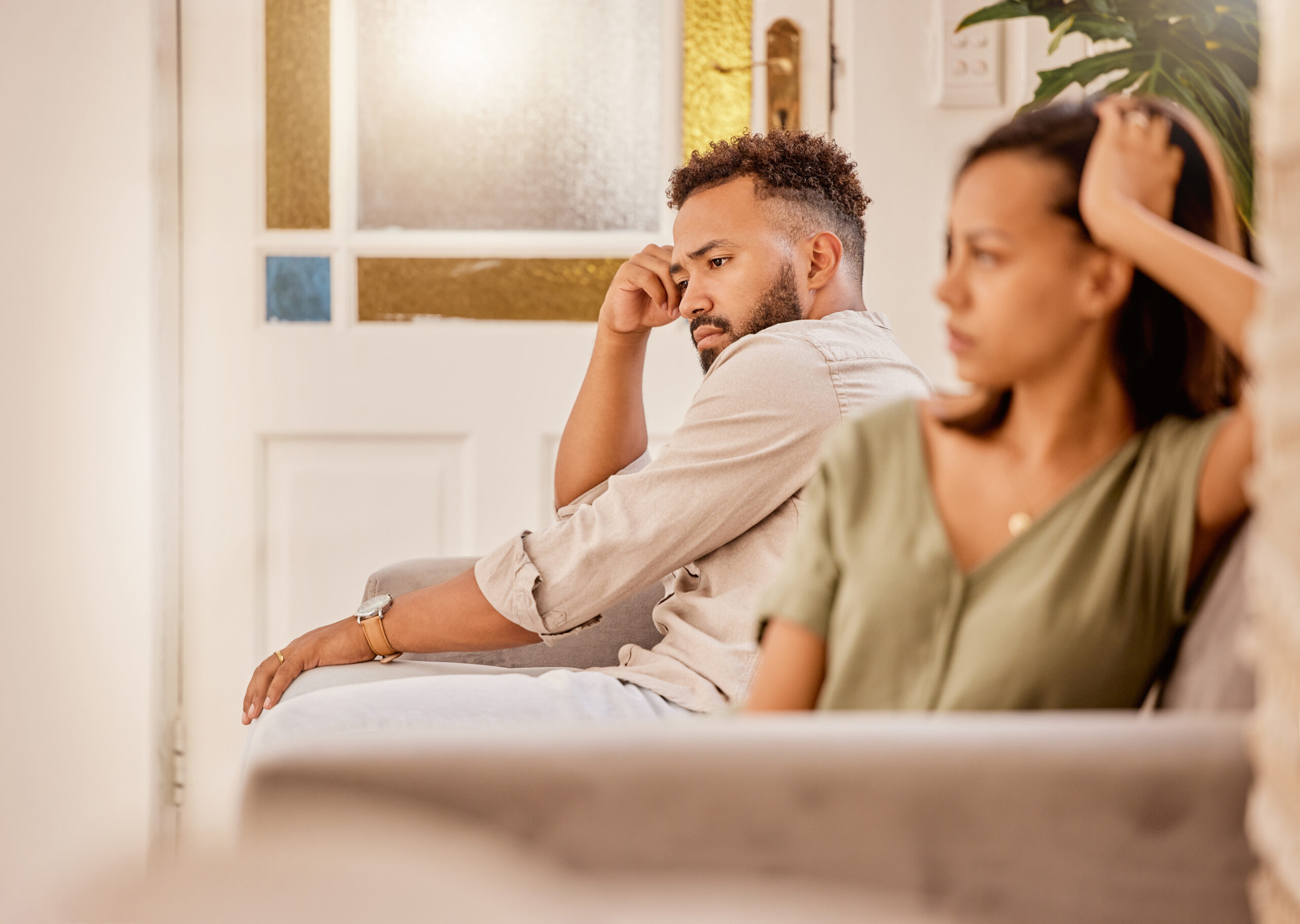 Two individuals sitting apart on a couch, both appearing contemplative and tense, highlighting scenarios where divorce mediation might not be recommended due to communication breakdown