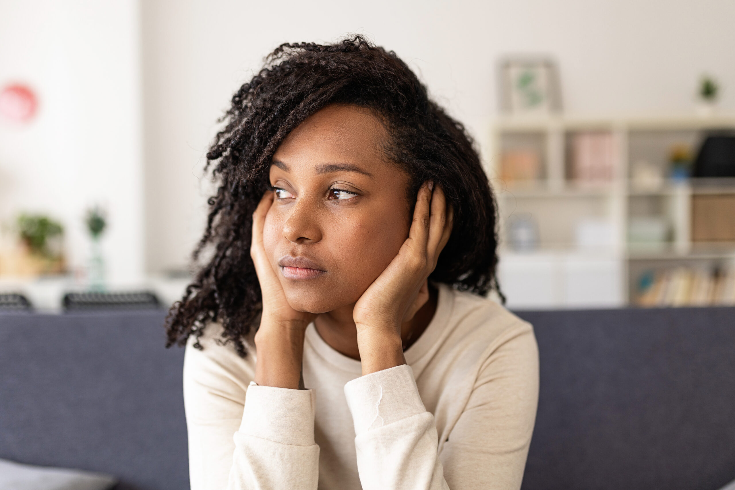 A thoughtful woman sitting on a sofa, appearing contemplative or sad, representing the emotional burden often associated with legal processes such as restraining orders and protective orders