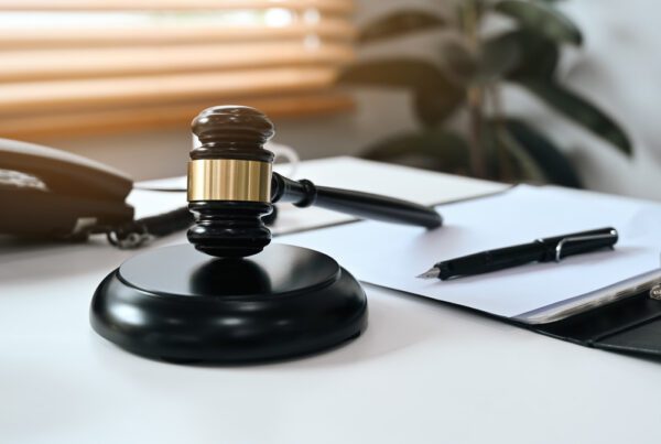 A judge's gavel rests on a desk alongside a pen and notepad, symbolizing legal proceedings and documentation