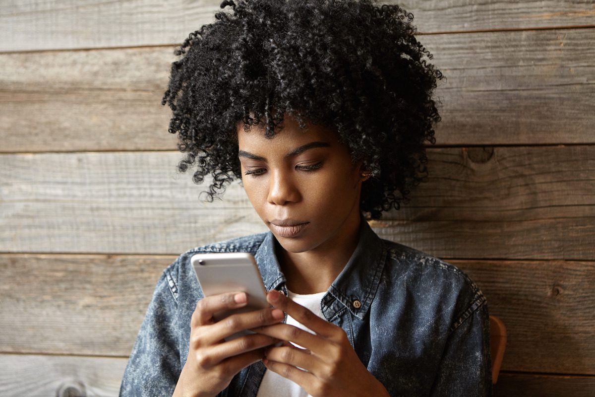 A woman with curly hair gazes at her phone, contemplating her next steps regarding a protective order's duration