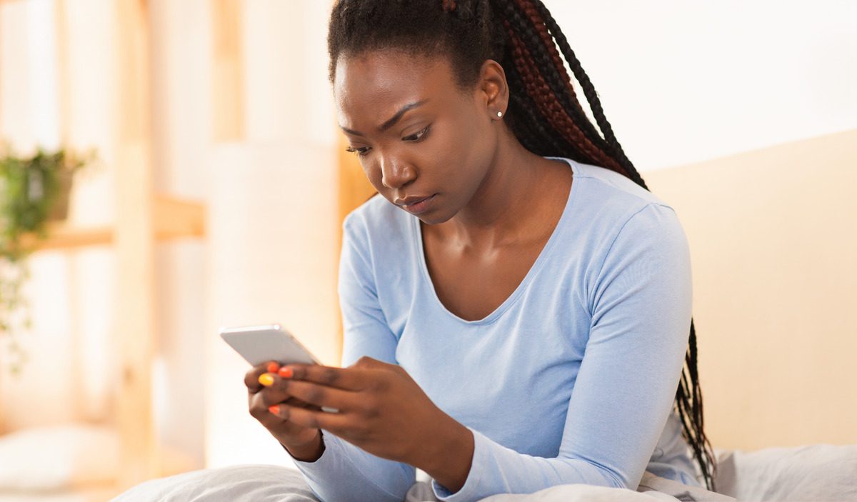 A woman sitting on a bed, focused on her phone, contemplating co-parenting and custody issues