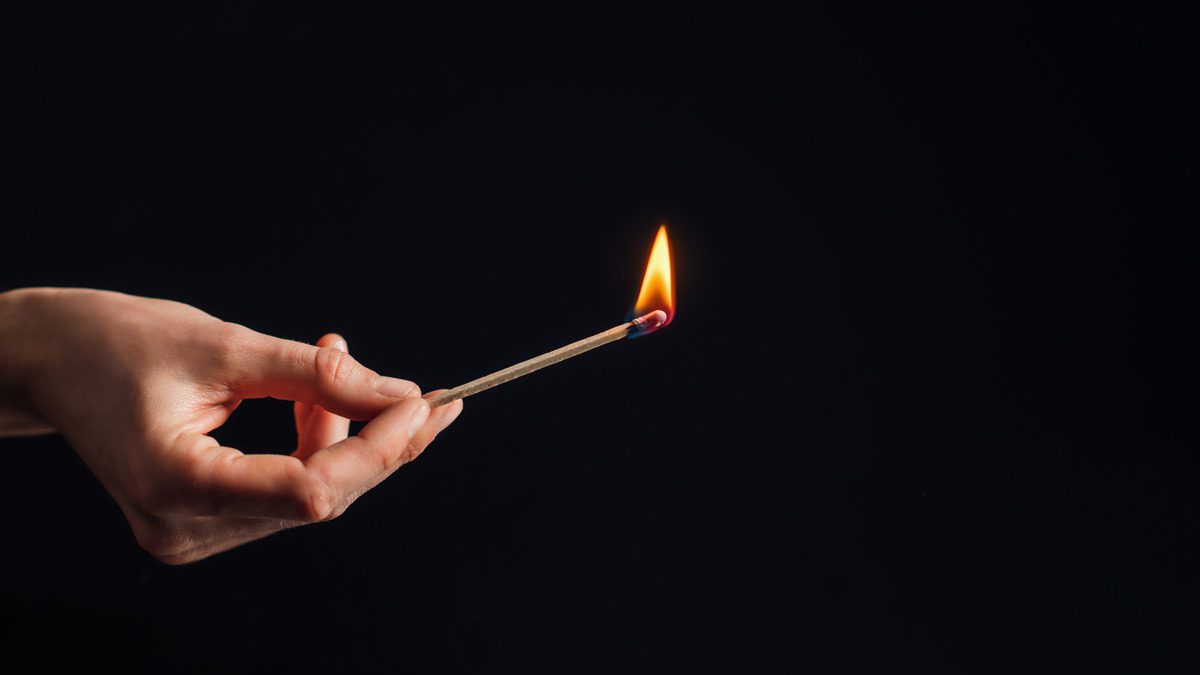 A person holding a matchstick against a black background, symbolizing the potential for fire and arson