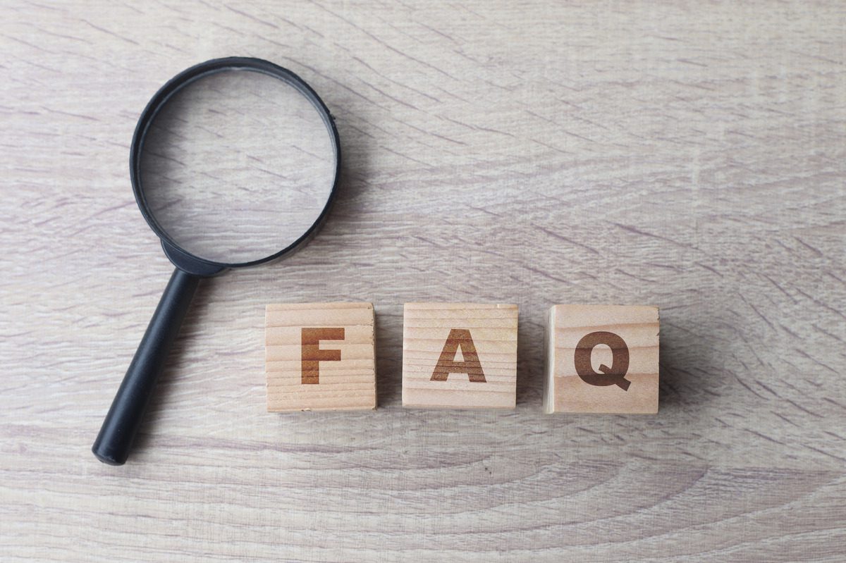 A magnifying glass rests on wooden blocks spelling "FAQ" on a wooden table, symbolizing inquiries about child support cessation