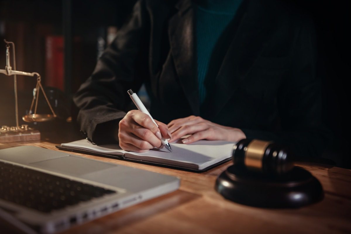 A lawyer diligently notes details in a notebook during a hearing in their office, preparing for a TRO discussion