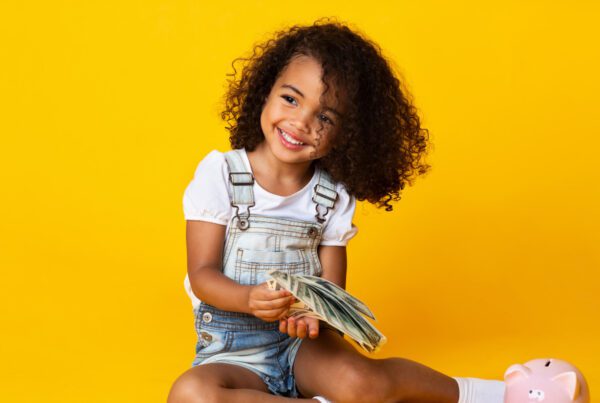 A young girl sits on the floor, focused on her piggy bank, symbolizing savings and financial responsibility