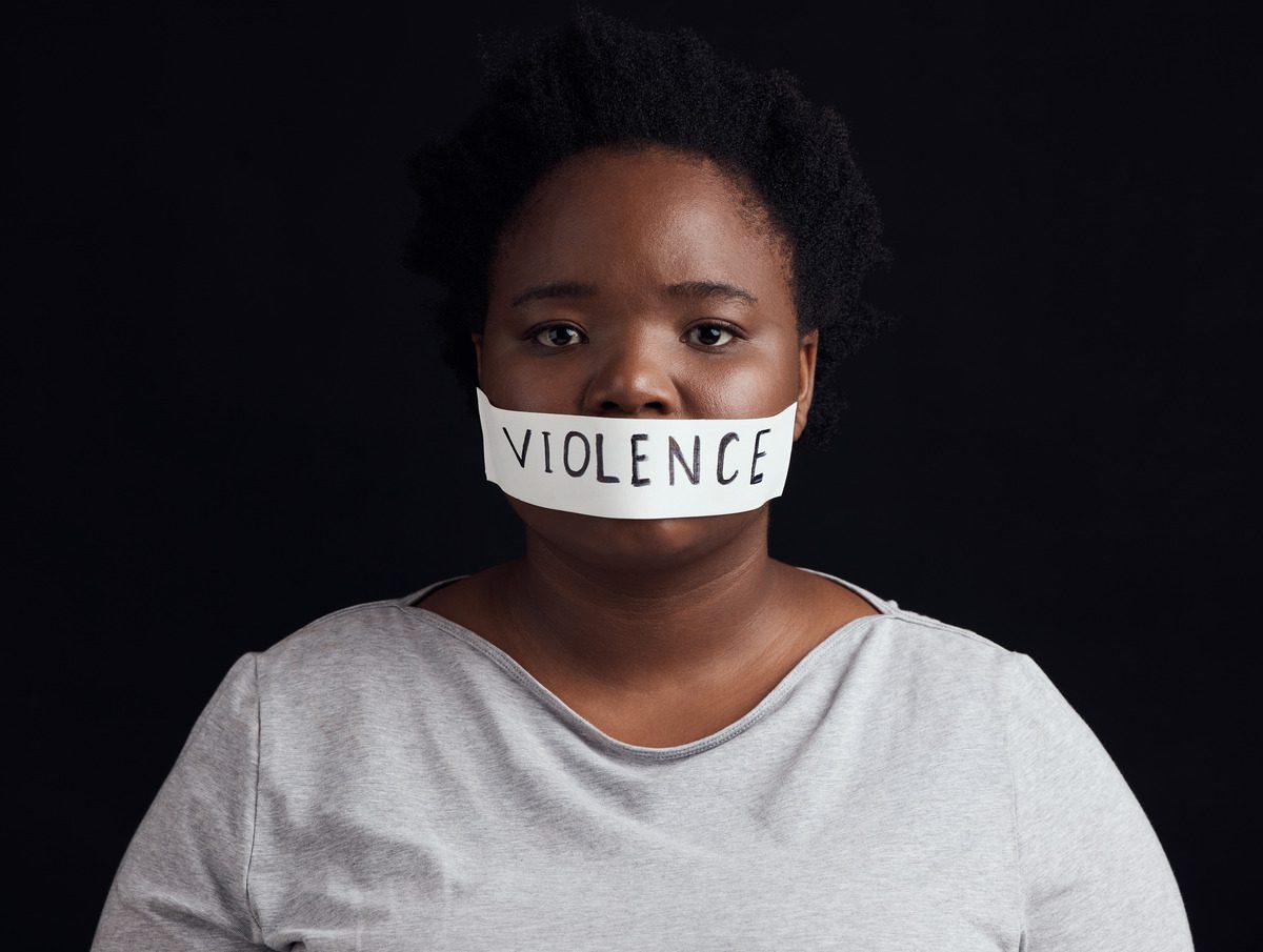 A woman with tape over her mouth labeled 'violence,' symbolizing the silence surrounding domestic abuse and restraining orders