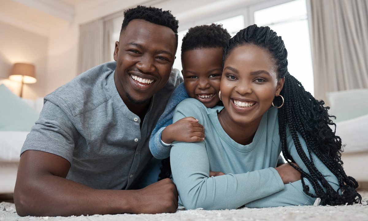 A joyful young black family smiles together while relaxing on a carpet, showcasing love and togetherness in their home