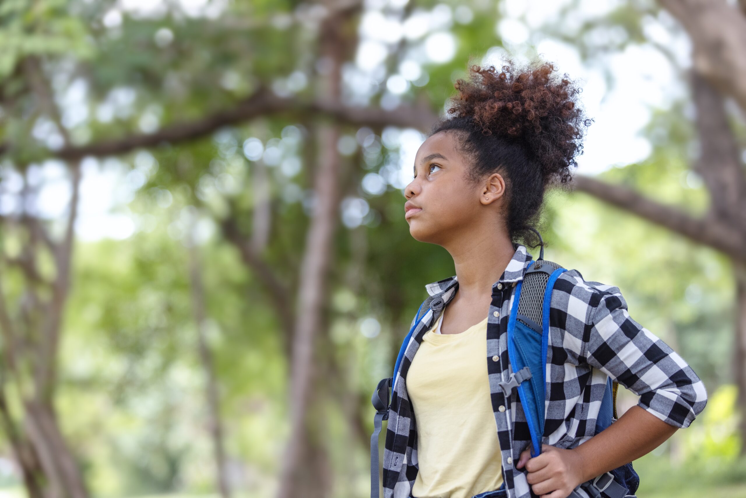 Young girl with backpack looking up thoughtfully in a peaceful forest setting