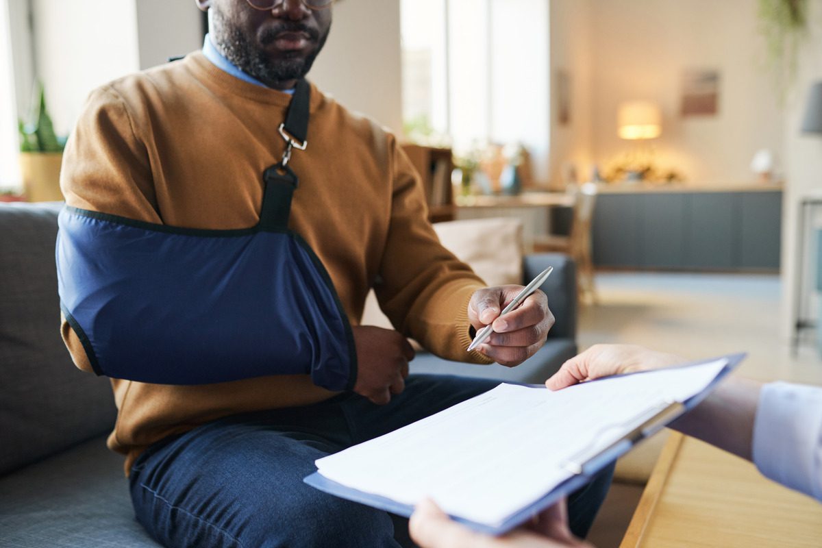 Injured man in an arm sling signing a personal injury claim or workers' compensation form, representing legal assistance for workplace accidents and medical insurance documentation