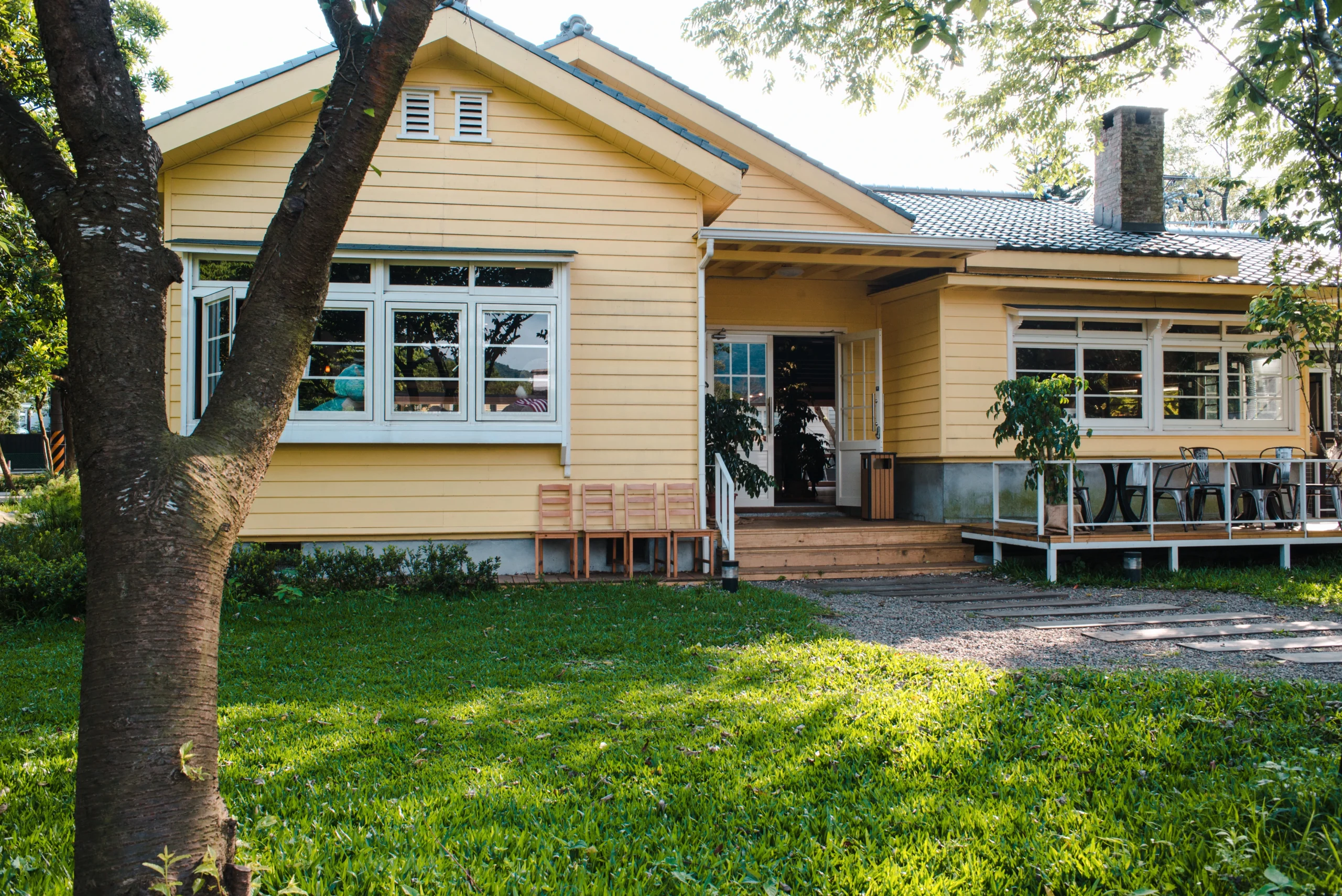 A cozy yellow house with a welcoming wooden porch and outdoor chairs, representing a peaceful home or cafe environment