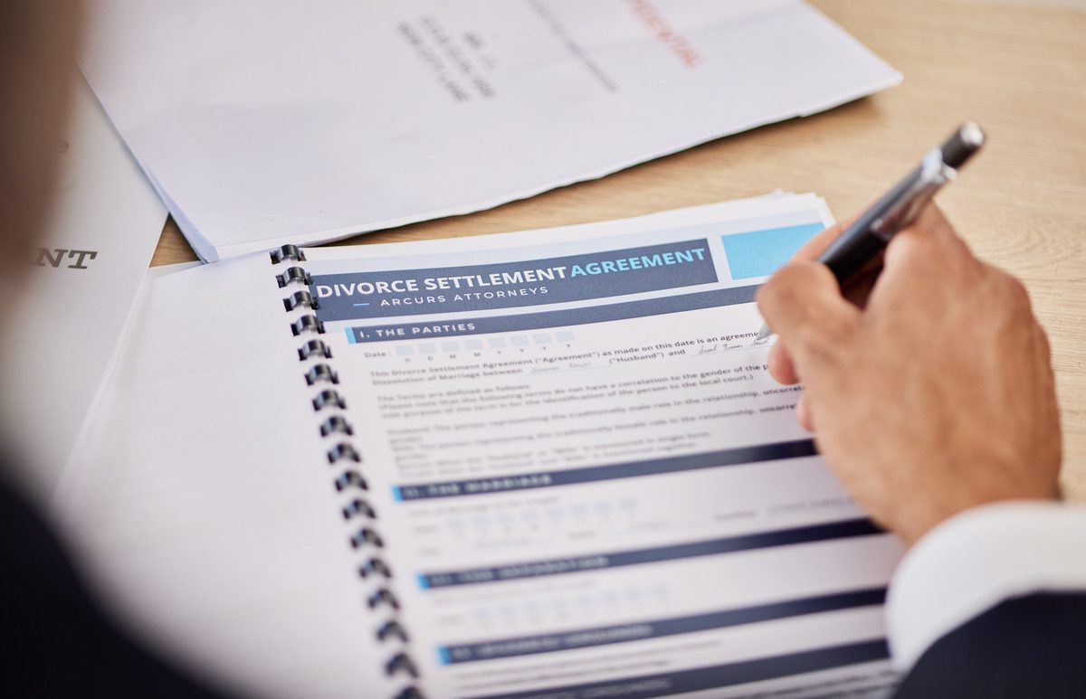 Hands holding a pen over a Divorce Settlement Agreement from Arcurs Attorneys, illustrating the final stages of a legal separation process