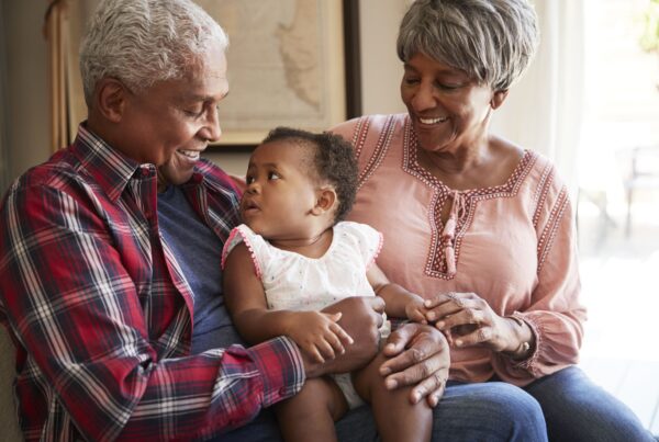 Grandparents smiling while holding baby indoors, representing family bonding, multigenerational love, childcare support, and happy family relationships