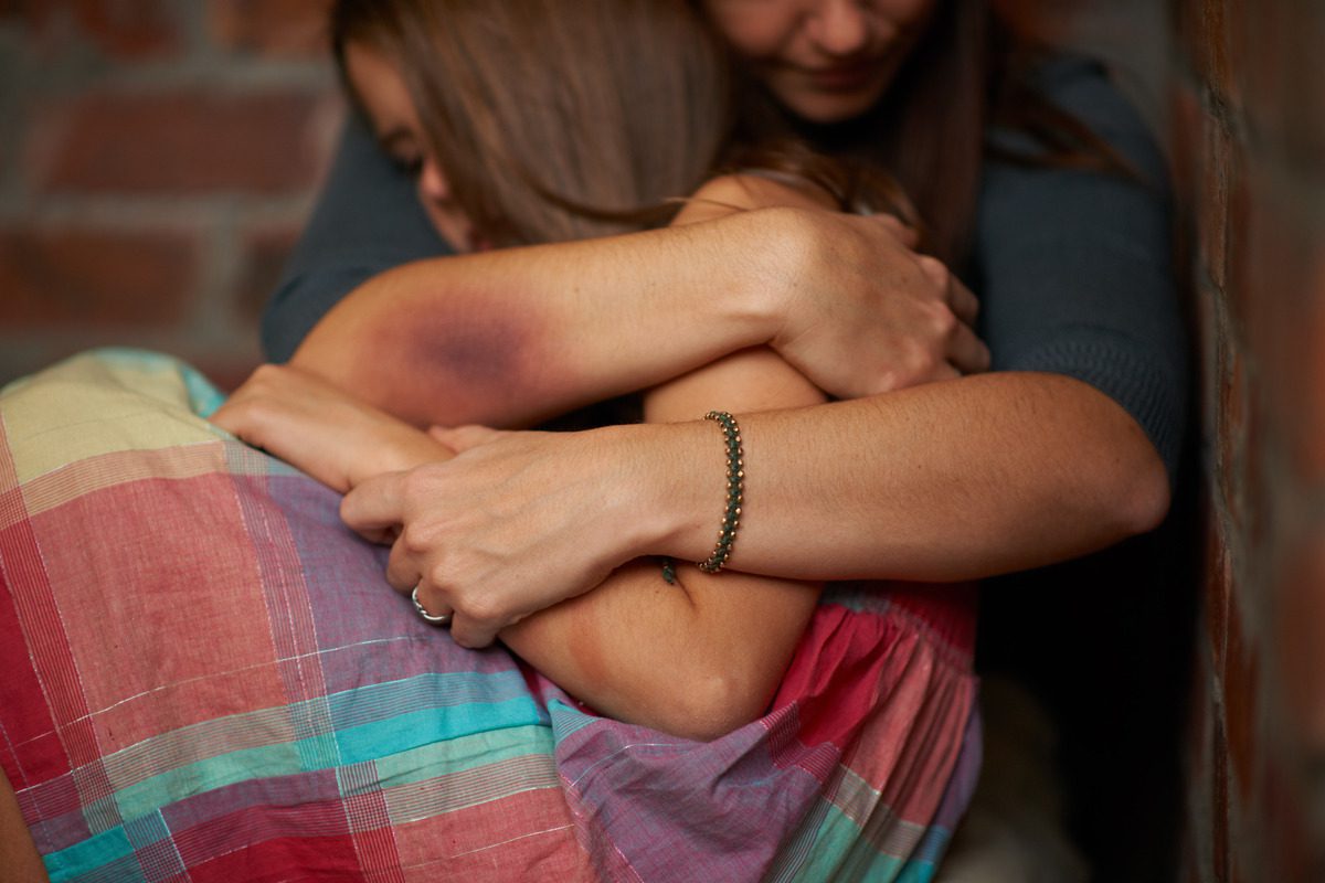Adult woman holding a young girl in a protective embrace to illustrate trauma recovery and emotional support for children