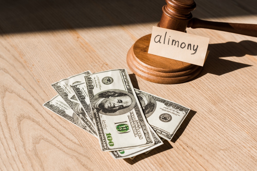 Alimony and family law concept with judge gavel and U.S. dollar bills on wooden table, representing spousal support payments, divorce settlements, and court-ordered financial obligations.