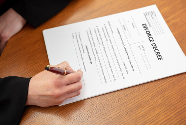 Person signing divorce decree document on wooden desk, representing legal separation, marriage dissolution, family law proceedings, and divorce paperwork completion