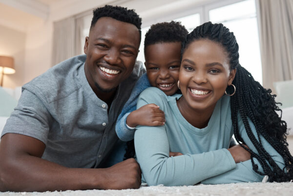 Happy family portrait with smiling parents and child lying together at home, representing family bonding, parental love, child well-being, and strong family relationships.