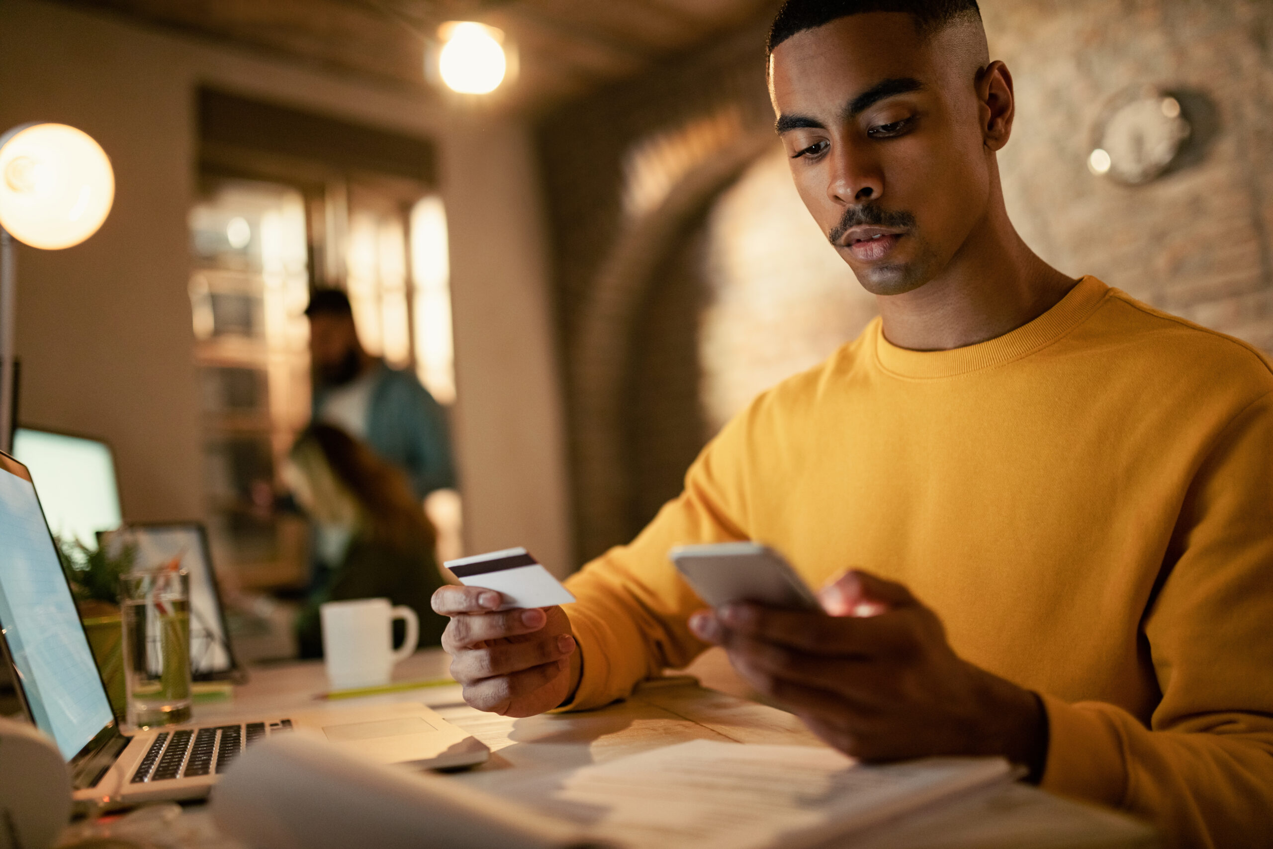 Person using smartphone and credit card while managing finances at desk, representing online banking, digital payments, e-commerce transactions, and secure mobile shopping