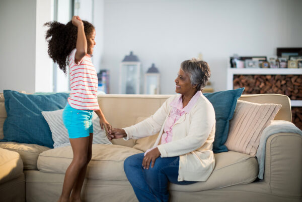 Grandparent and child holding hands and smiling in a living room, symbolizing kinship adoption, family support, child welfare, multigenerational caregiving, and a loving home environment.