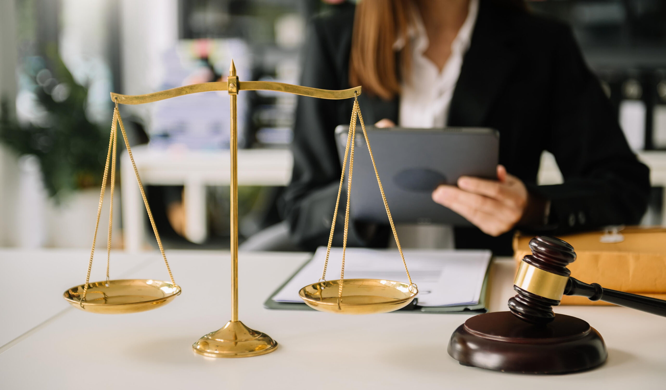 Scales of justice and a judge's gavel on a lawyer’s desk with a legal professional in the background, symbolizing family law services, legal consultation, court proceedings, and professional legal representation.