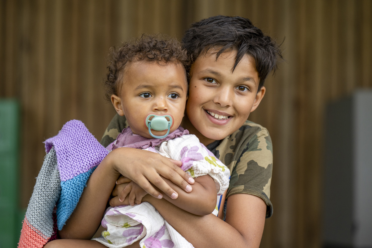 Older child lovingly holding a younger sibling outdoors, symbolizing sibling adoption, foster care, family bonding, child welfare, and the importance of keeping brothers and sisters together in permanent adoptive homes